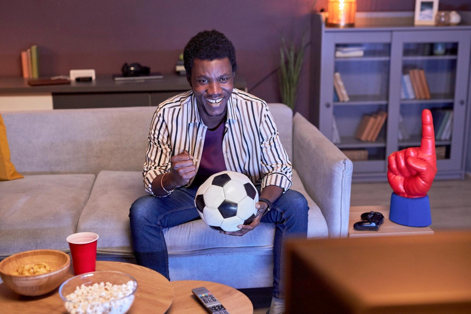 Homem segura bola assistindo futebol na TV